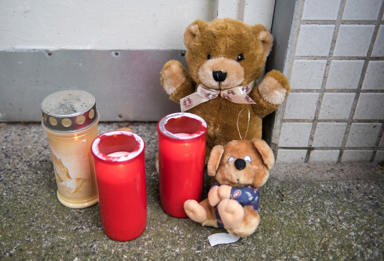 Kerzen und Teddybären aus Stoff stehen vor einem Mehrfamilienhaus in Hamburg. Dort wurde ein zweijähriges Mädchen getötet.