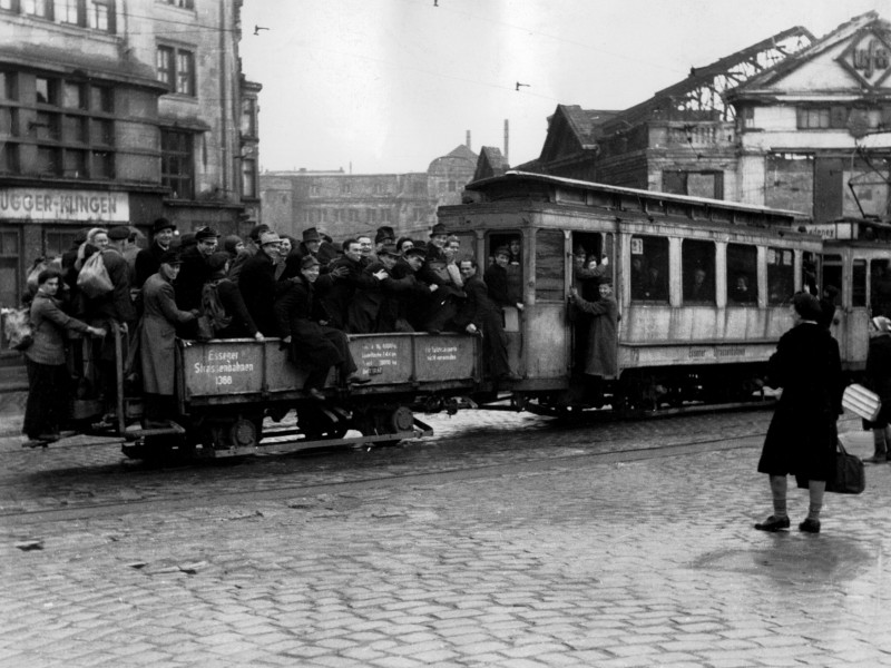 Auf der Viehofer Straße: Links das Allbauhaus, das den Krieg halbwegs heil überstanden hat. Es beherbergte das alteingesessene Haushaltswarengeschäft Dellbrügger und Klingen. Mangels einsetzbarer Wagen mussten Fahrgäste mit Behelfskonstrukten Vorlieb nehmen. Die Fröhlichkeit irritiert angesichts der zerbombten Umgebung. Aber man hatte ja immerhin überlebt.