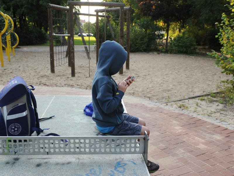 Ein Junge sitzt mit seinem Schulranzen auf einer Tischtennisplatte.