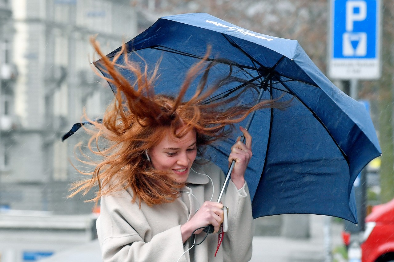 Eine junge Frau mit Regenschirm kämpft im Regen gegen den Wind an. 