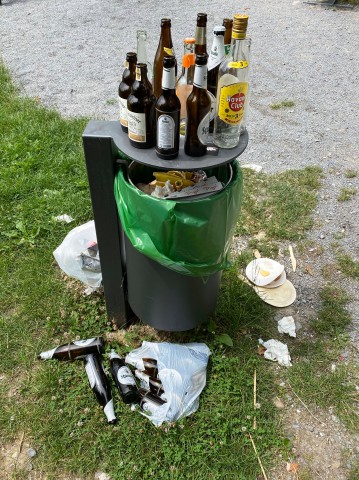 Ein übervoller Mülleimer, mit viel Müll, Glasflaschen daneben. (Symbolbild)