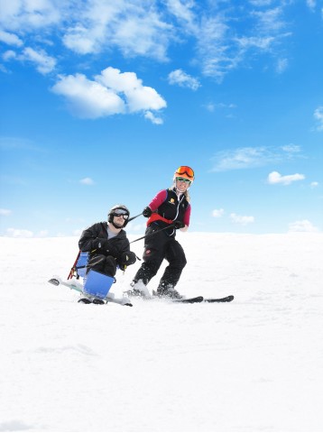 Wer aufgrund seiner Behinderung nicht allein auf die Piste kann, für den bieten sich Bi-Ski an. Hier lenkt ein Begleiter den Hang hinab. 