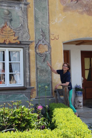 Regine Ronge zeigt die Lüftlmalerei an einer Hauswand in Mittenwald.