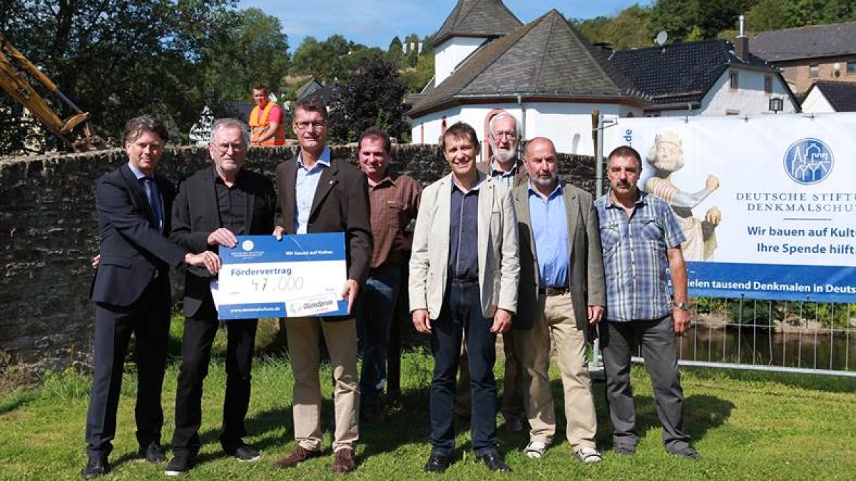 Endlich ist es soweit: Die Brigida-Brücke im malerischen Eifel-Ort Kronenburg wird saniert. Hier im Bild:  Jan Lembach, Bürgermeister der Gemeinde Dahlem (3. von links) freut sich über die großzügige Fördersumme von 47.000 Euro, überbracht von Wolf Werth, Ortskurator der Deutschen Stiftung Denkmalschutz (2. von li.) und WestLotto-Bezirksleiter Andre Bentz (1. von li.).