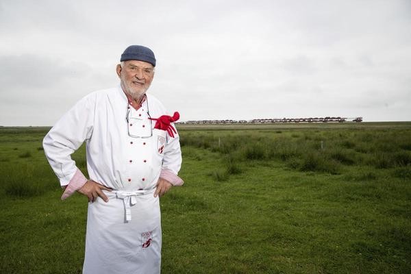 Jürgen Gosch, Fischhändler und Gastronom, steht auf einer Wiese neben dem Hindenburgdamm auf Sylt bei Morsum vor einem vorbeifahrenden Autozug. 