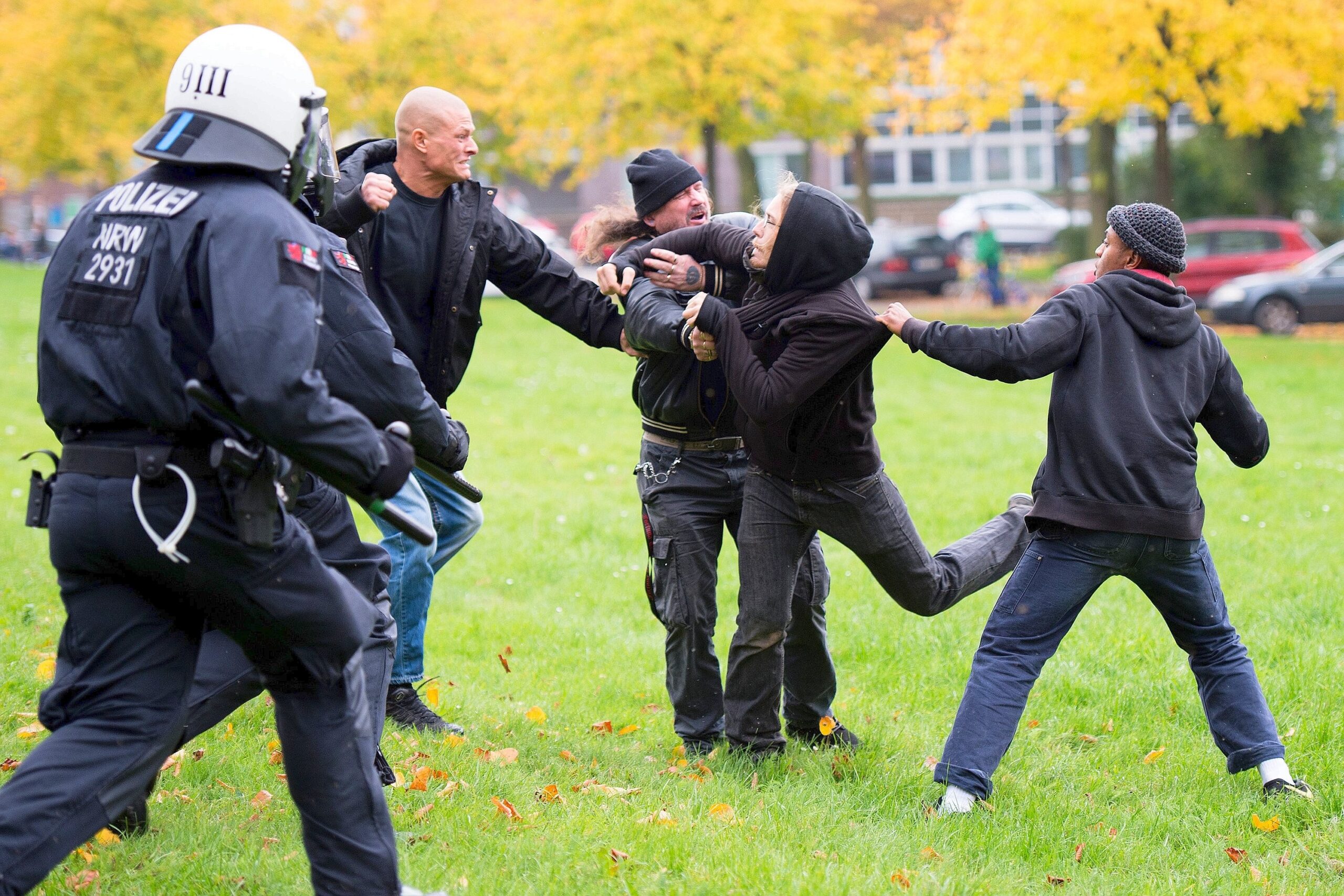 Teilnehmer der Hogesa-Demonstration und Gegendemonstranten gehen auf einer Wiese vor der Lanxess-Arena aufeinander los.