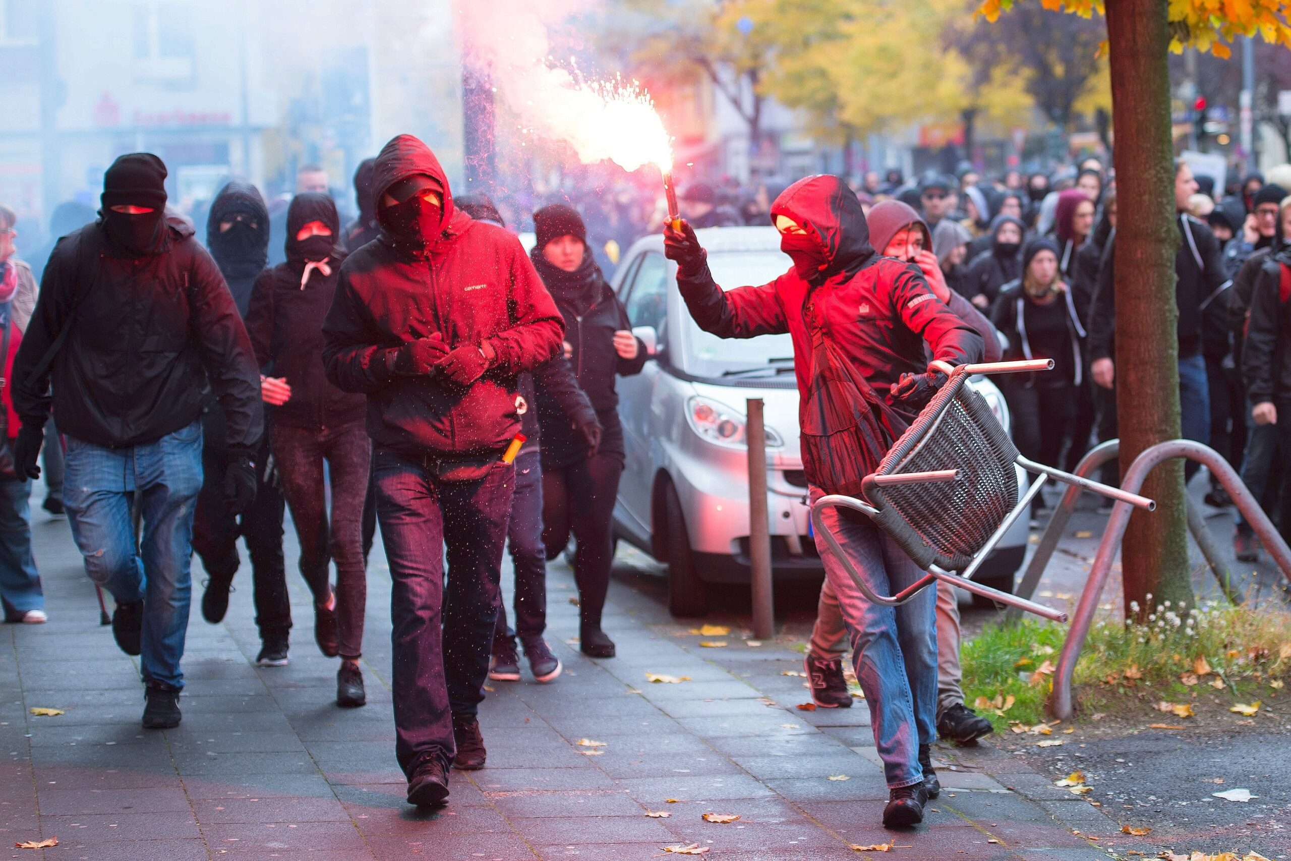 Mitglieder der Antifa laufen mit einer Bengalischen Fackel in der Hand durch eine Straße in Köln.