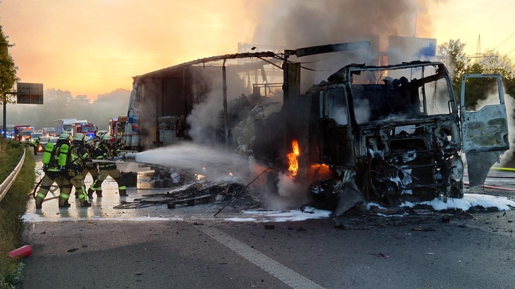 Auf der A1 brennt ein LKW lichterloh. Feuerwehrmänner versuchen die Flammen zu löschen.