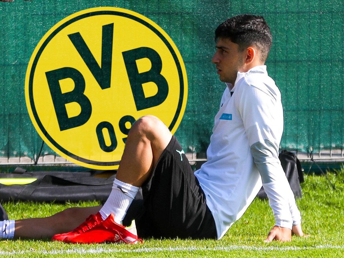 Yusuf Demir sitzt am Boden und schaut auf das Wappen von Borussia Dortmund.