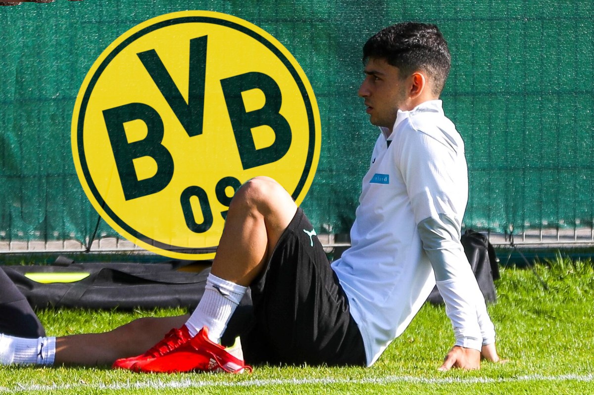 Yusuf Demir sitzt am Boden und schaut auf das Wappen von Borussia Dortmund.