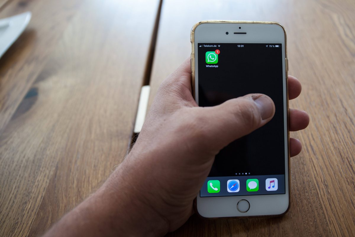 Eine Hand liegt auf einem Tisch und hält ein Smartphone in der Hand, auf dem die App Whatsapp zu sehen ist.