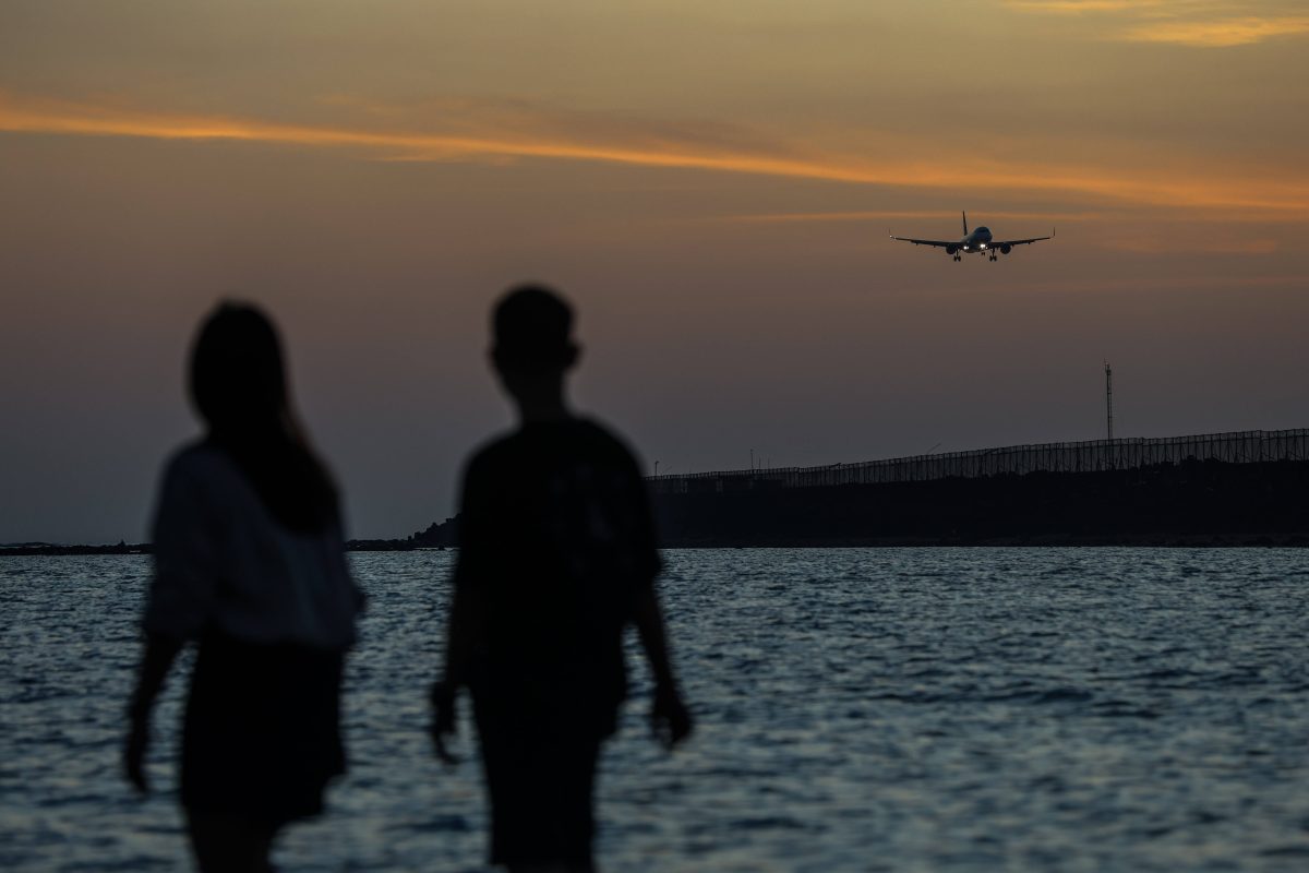 Touristen am Strand von Bali vor einem Sonnenuntergang und einem tieffliegenden Flugzeug