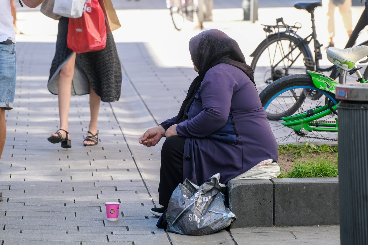 Frau sitzt auf der Straße und bettelt