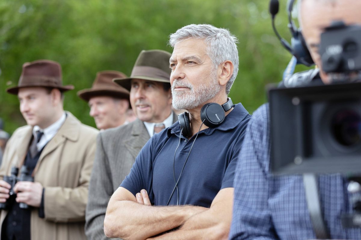 Schauspieler George Clooney. Er trägt schwarze Kopfhörer um den Hals und hat ein blaues Polo-T-Shirt an.