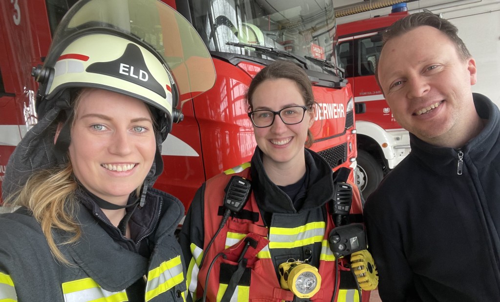 2 Feuerwehrleute und unsere Reporterin Chaleen vor einem Feuerwehrauto