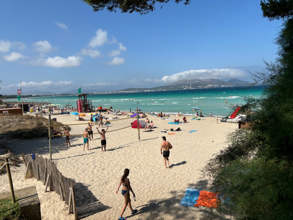 Menschen, die am Playa de Muro Beachvolleyball und die Natur einer der schönsten Strände Mallorcas genießen, umgeben von Dünen und klarem Wasser.