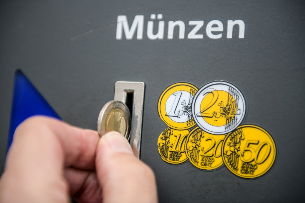 Eine Hand wirft eine 2-Euro-Münze in den Schlitz eines Münzeinwurfes als Symbol für Gebühren auf Kleinanzeigen.