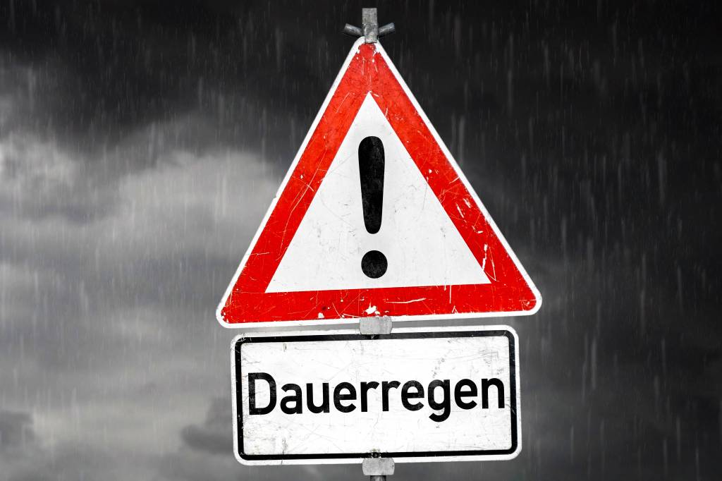 Ein Warndreieck warnt vor grauer und regnerischer Wolkendecke vor Dauerregen.